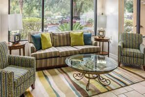 Una sala de estar con sofá, sillones, una mesa de centro de vidrio y vistas al exterior a través de amplios ventanales.