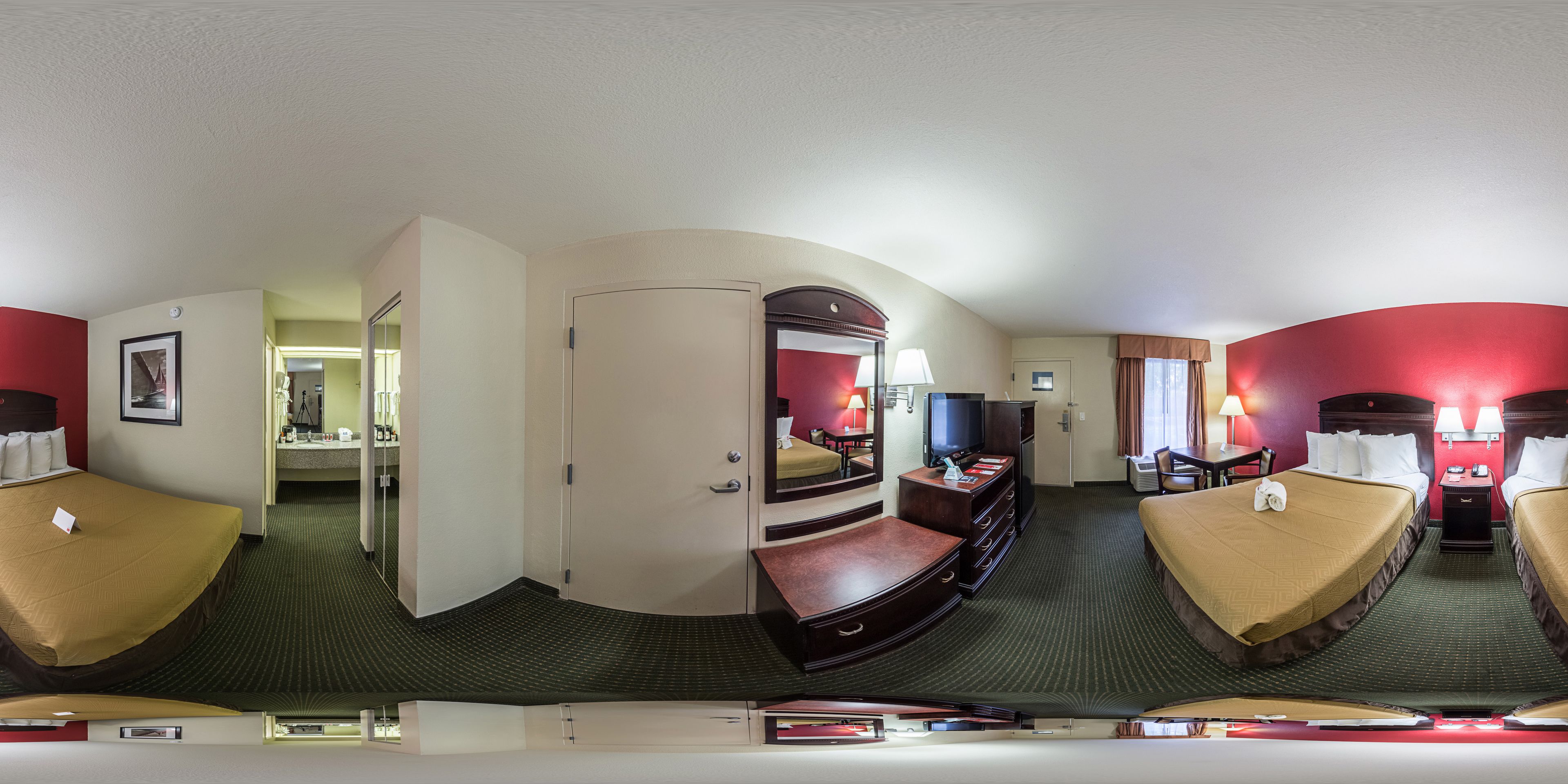 Habitación de hotel con dos camas, televisión, escritorio y baño visible a través de una puerta abierta.
