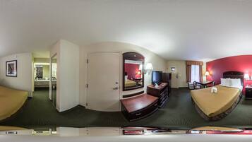 Habitación de hotel con dos camas, televisión, escritorio y baño visible a través de una puerta abierta.