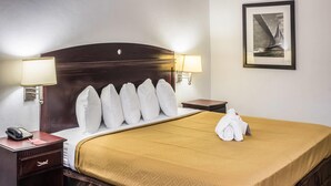 Habitación de hotel con una cama grande, dos lámparas de noche, una mesita de noche con un teléfono, un cuadro en la pared y una cama bien hecha con toallas.