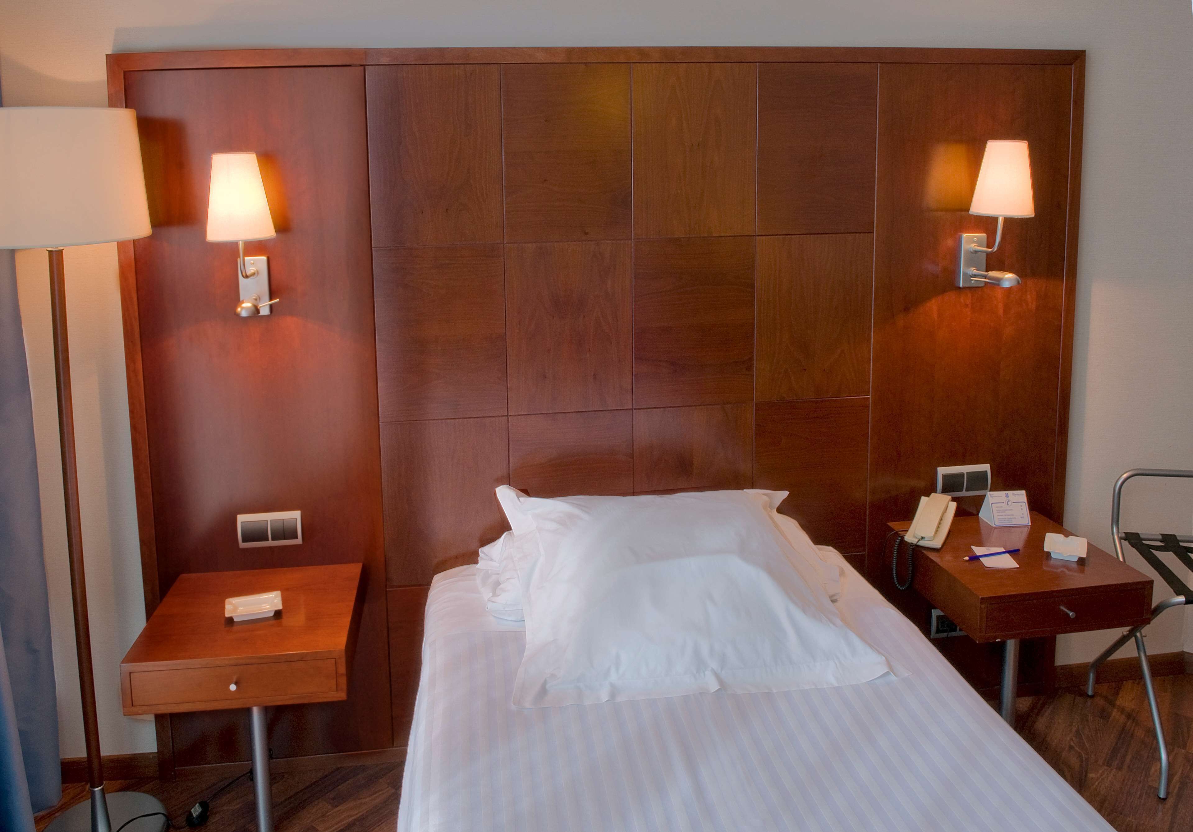 A hotel room with a large bed, two bedside tables with lamps, a desk with a telephone, and a chair.