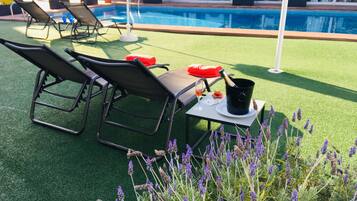 A poolside area with lounge chairs, a table with a bottle of champagne, and a glass of wine.