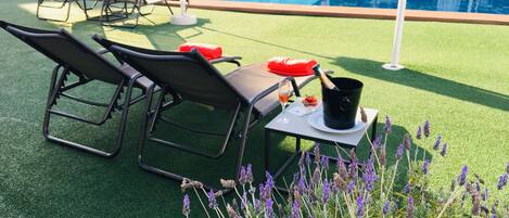Zona junto a la piscina con sillones de descanso, una mesa con una botella de champán y una copa de vino.