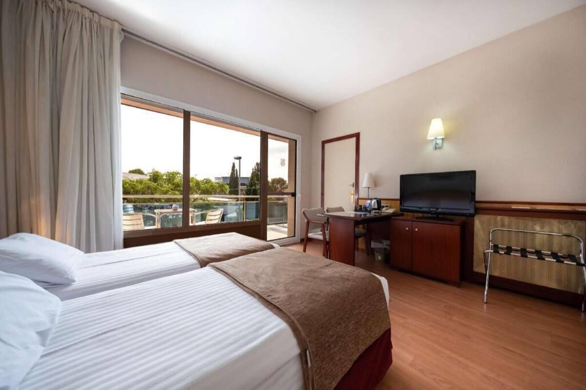 Une chambre d’hôtel avec deux lits, un bureau, une télévision, une chaise et une vue sur l’extérieur.
