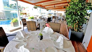 Un comedor con mesas redondas dispuestas para una comida, rodeado de sillas de mimbre y vistas a una piscina.
