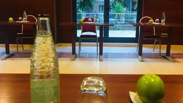 A hotel room with a wooden table, a bottle of water, a glass, a green apple, and a pen on a notepad.