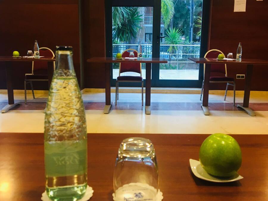 A hotel room with a wooden table, a bottle of water, a glass, a green apple, and a pen on a notepad.