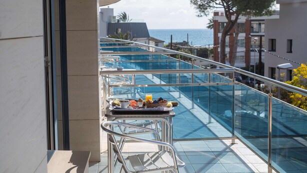 Un balcón con barandilla de cristal que da a una piscina y al mar.