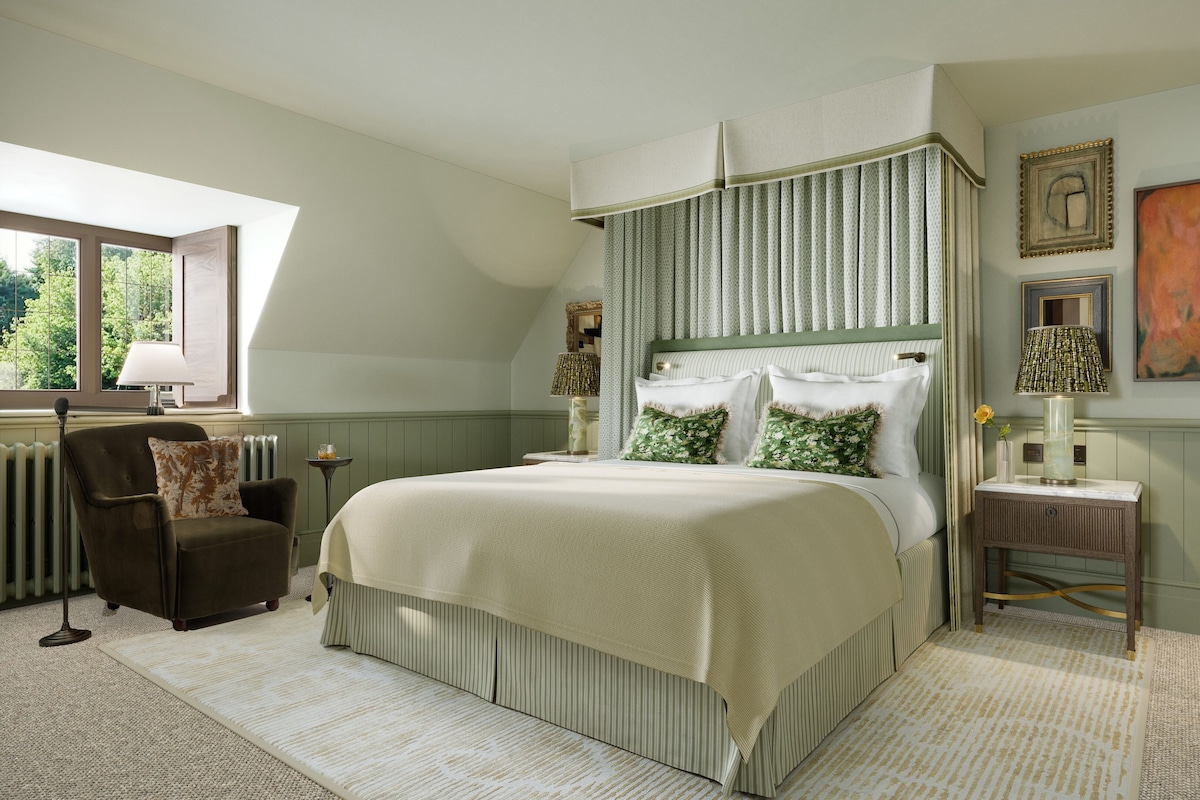 Une chambre à coucher avec un grand lit, une chaise, une table de chevet, une lampe et une fenêtre.