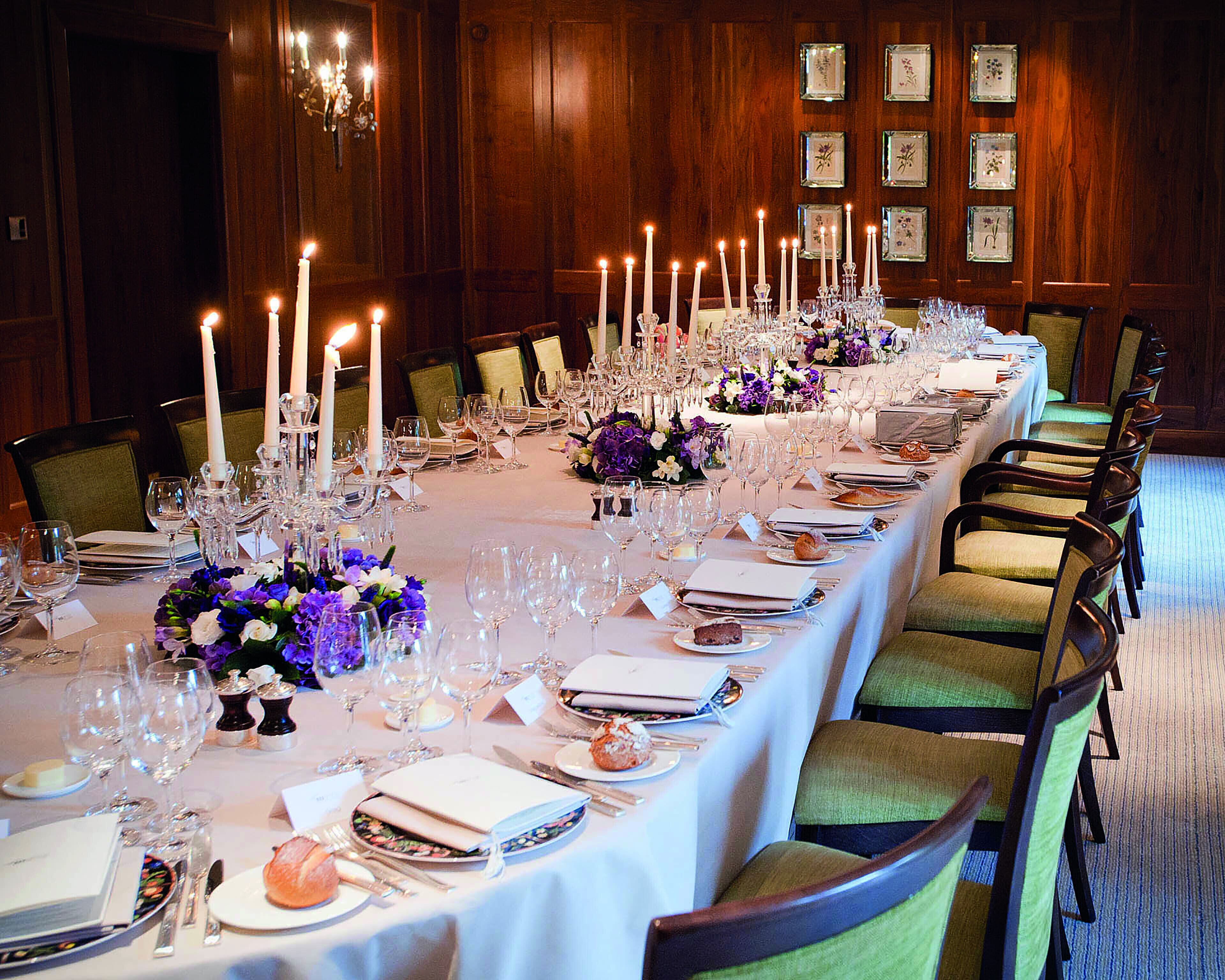 Una larga mesa de comedor dispuesta con numerosas velas, copas y centros de mesa florales.