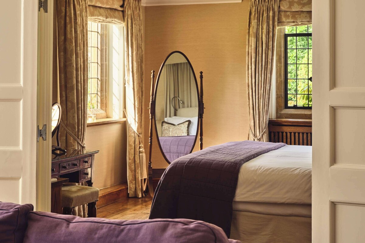 Un dormitorio con cama, una silla, un aparador y una ventana con cortinas.
