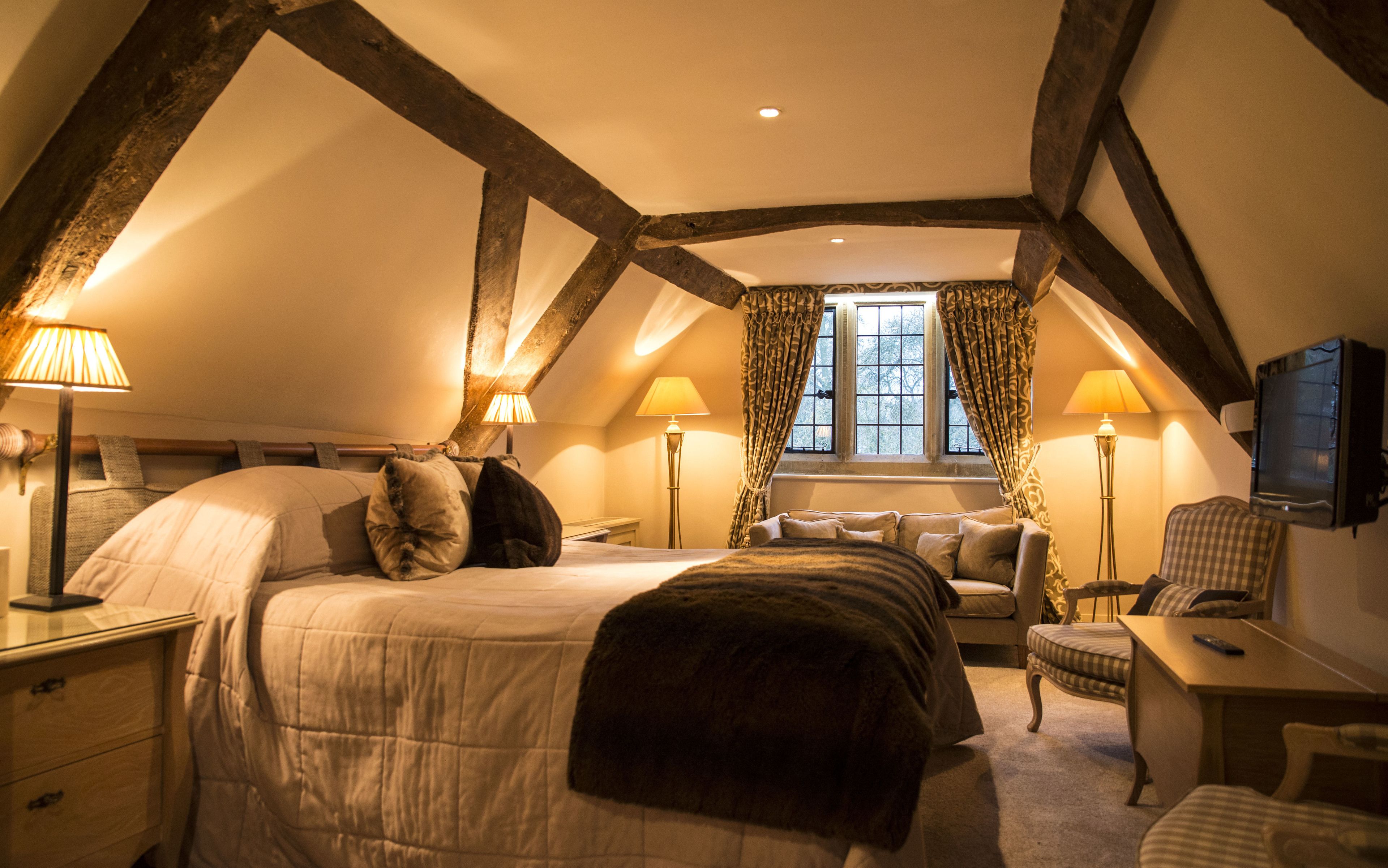 A cozy attic bedroom with a large bed, two bedside tables, a chair, a desk, and a television.