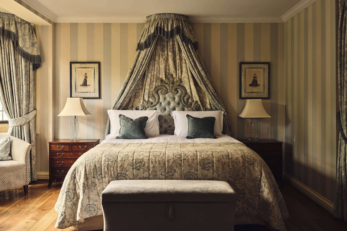 Quarto com cama de dossel, papel de parede listrado e duas imagens emolduradas na parede.