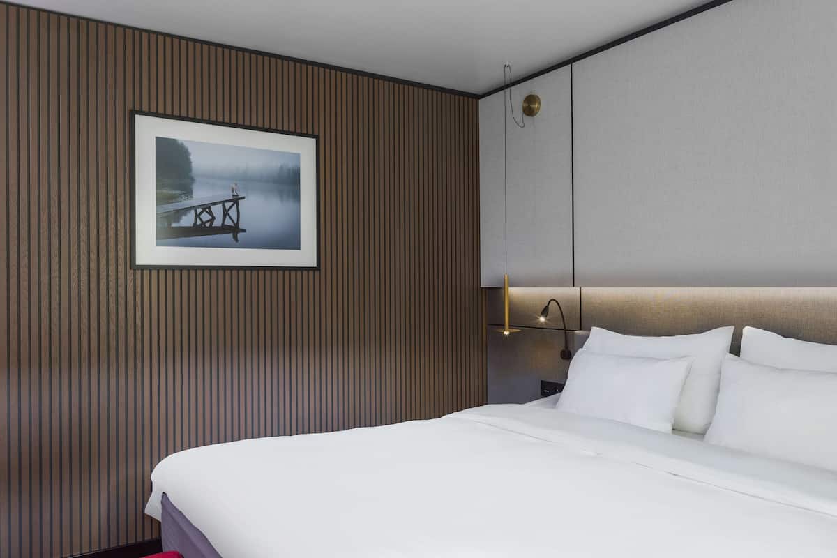 Une chambre d’hôtel avec un grand lit, un tableau encadré au mur et une table de chevet avec une lampe.