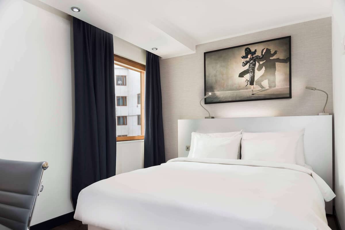 Une chambre d’hôtel avec un grand lit, un bureau et une fenêtre avec des rideaux.