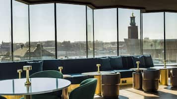 A modern lounge with a panoramic city view, featuring a curved seating area with round tables and chairs.
