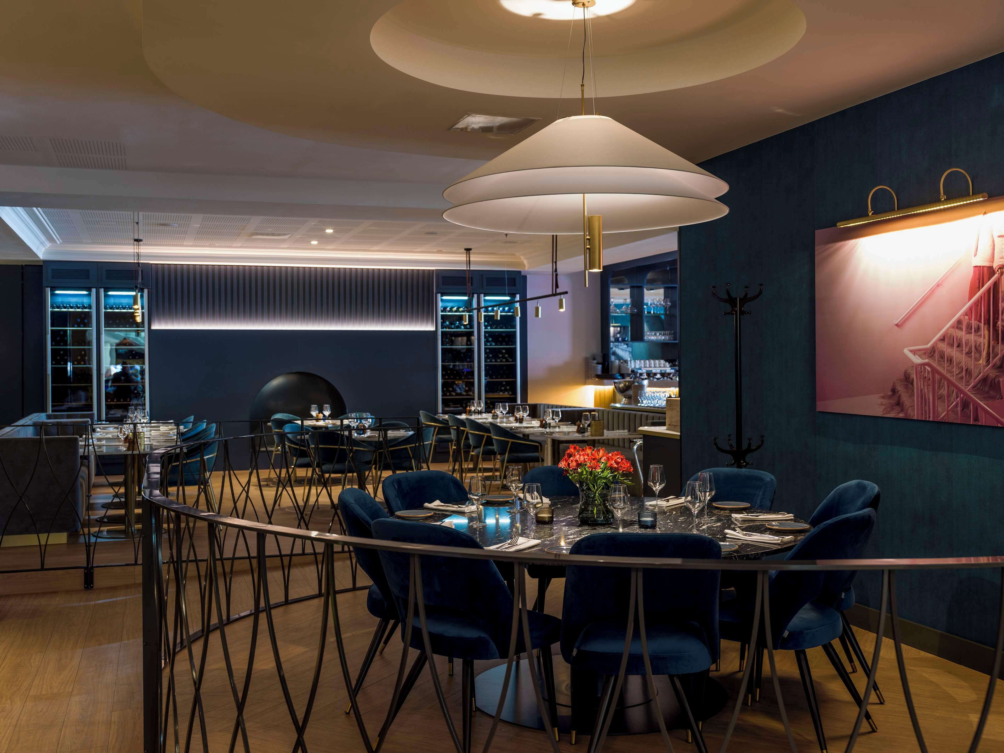A modern dining area with round tables, blue upholstered chairs, and a large pendant light.