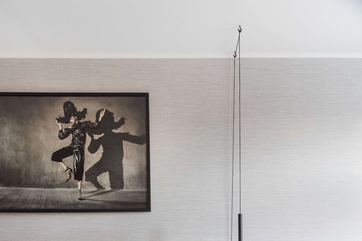 Une chambre à coucher moderne avec un grand lit, une table de chevet avec une lampe et une œuvre d’art encadrée au mur.