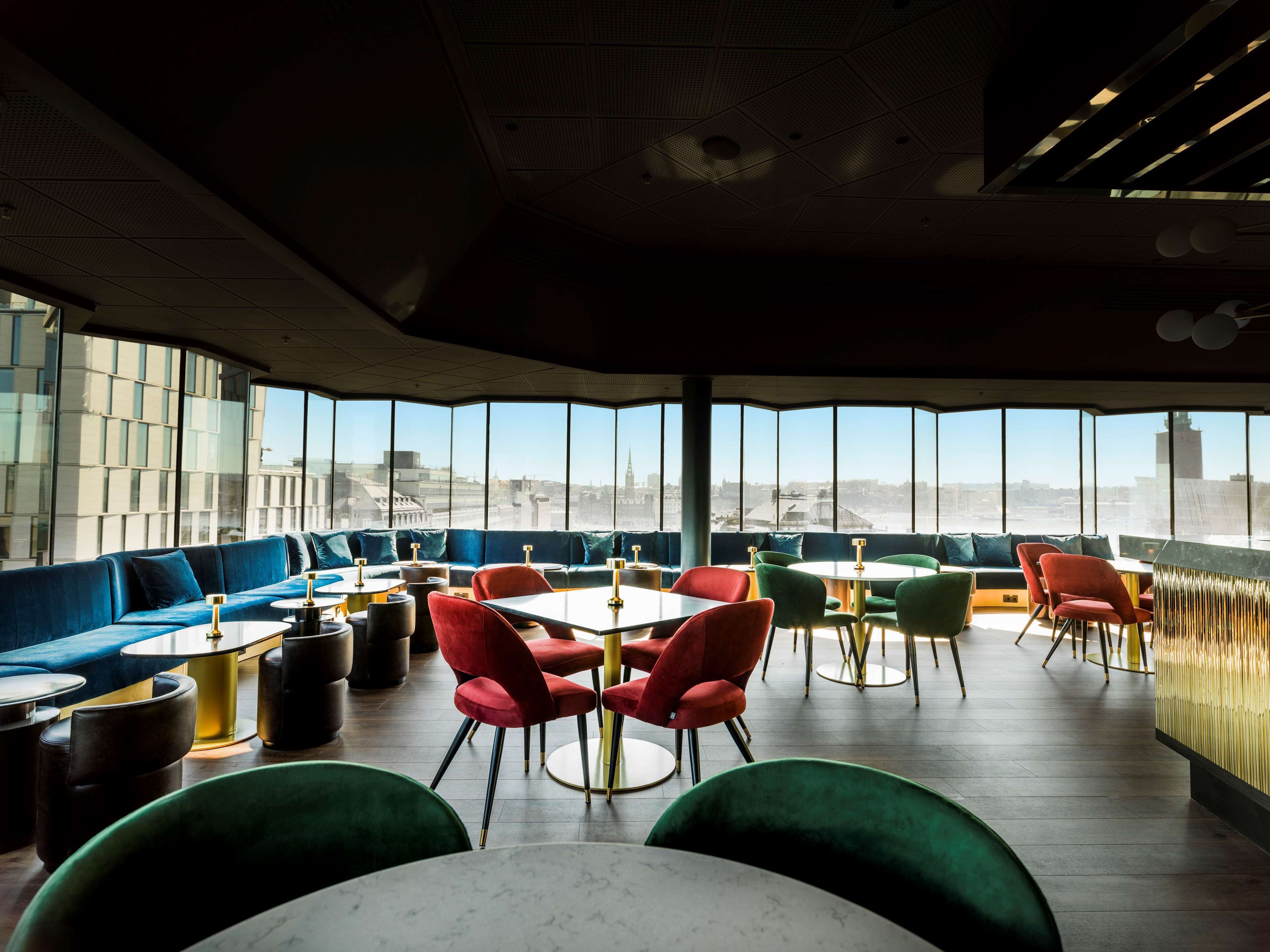 Un restaurante moderno con techos altos, ventanas amplias y diversas opciones de asientos, incluyendo cabinas y mesas.