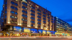 Ett hotell med flera våningar, utformat i modern arkitektonisk stil, med en framträdande glasfasad och flera flaggor på taket.