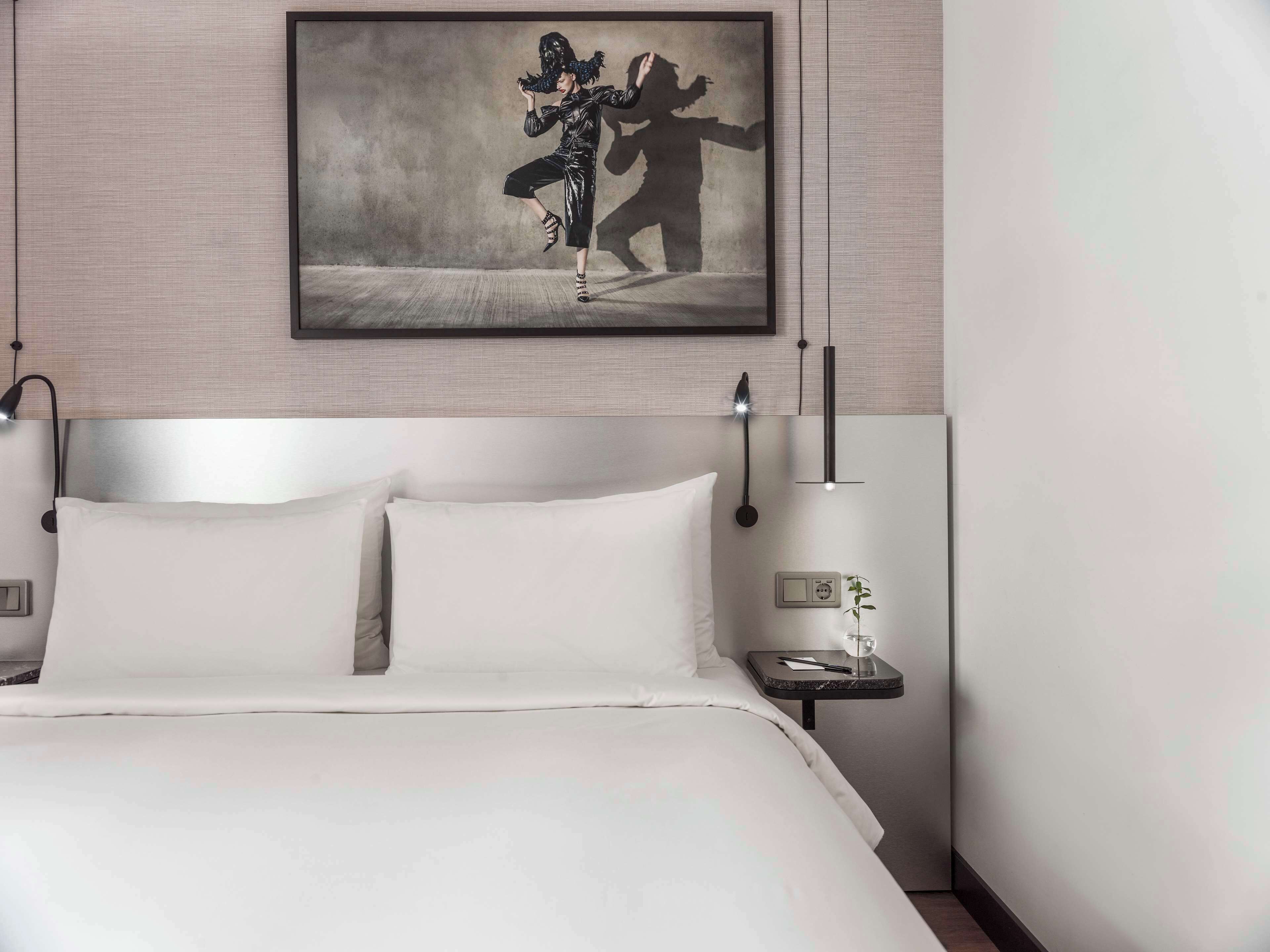 A hotel room with a large bed, two bedside tables, a wall-mounted artwork, and a nightstand with a lamp.