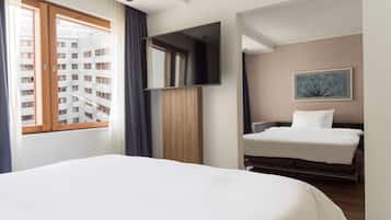 Ett hotellrum med en stor säng, en mindre säng, en tv som är monterad på väggen och ett fönster med gardiner.