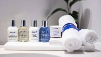 A bathroom counter with various personal care products including shampoo, conditioner, body wash, and a shower cap.