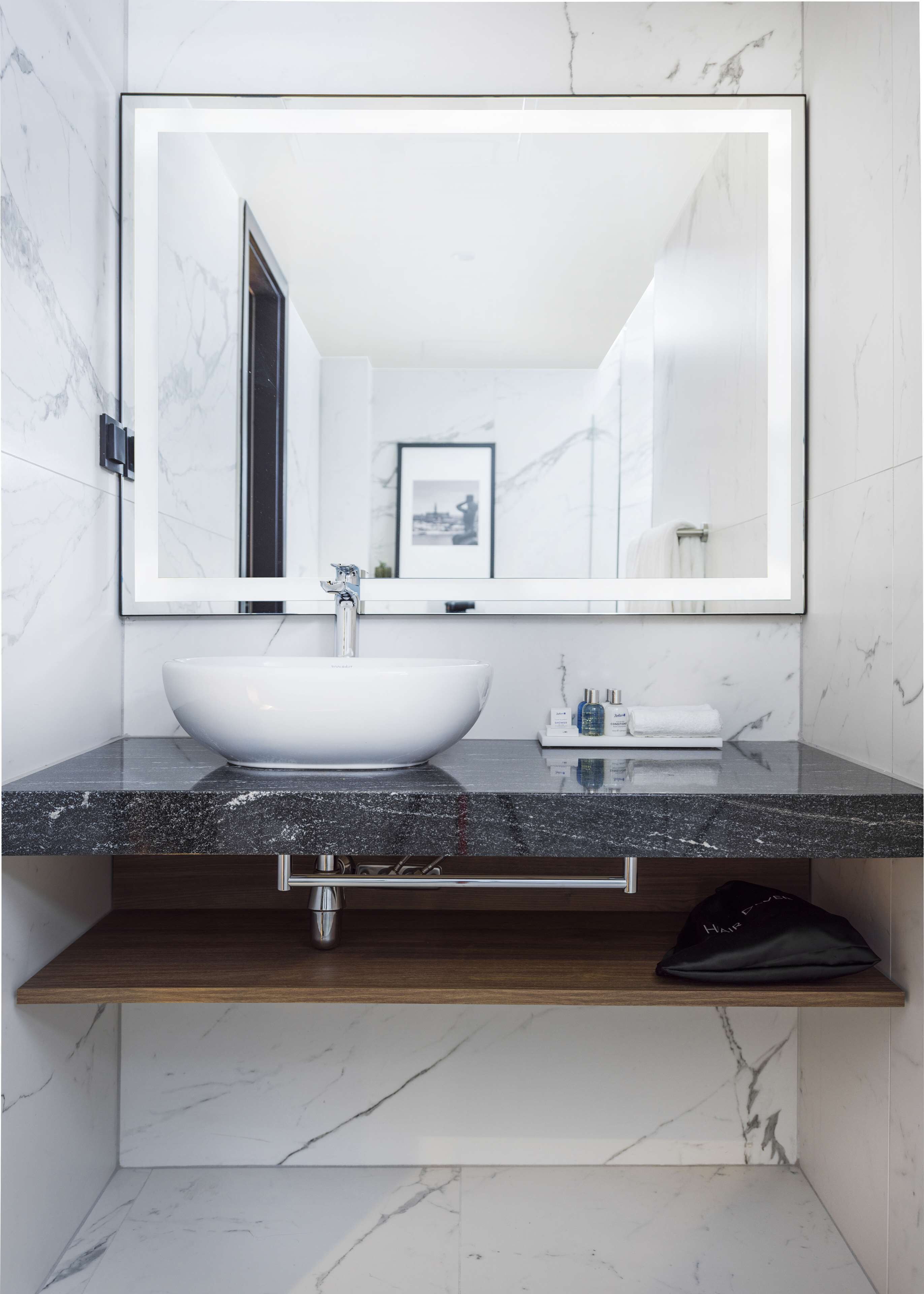 Un baño moderno con un lavamanos de mármol blanco, un espejo grande y un cuadro en la pared.