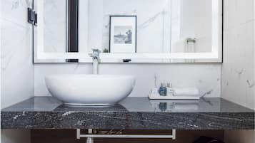 Un baño moderno con un lavamanos de mármol blanco, un espejo grande y un cuadro en la pared.