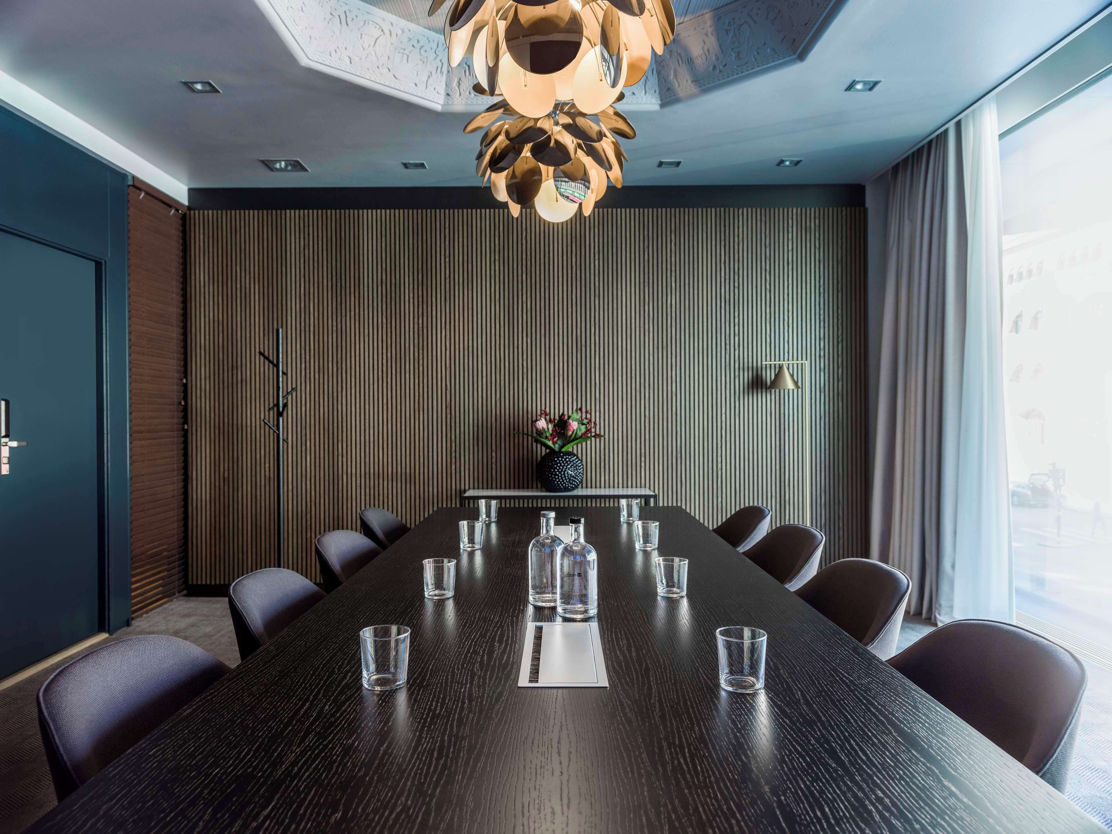 A conference room with a long table, chairs, a vase with flowers, and a modern ceiling design.