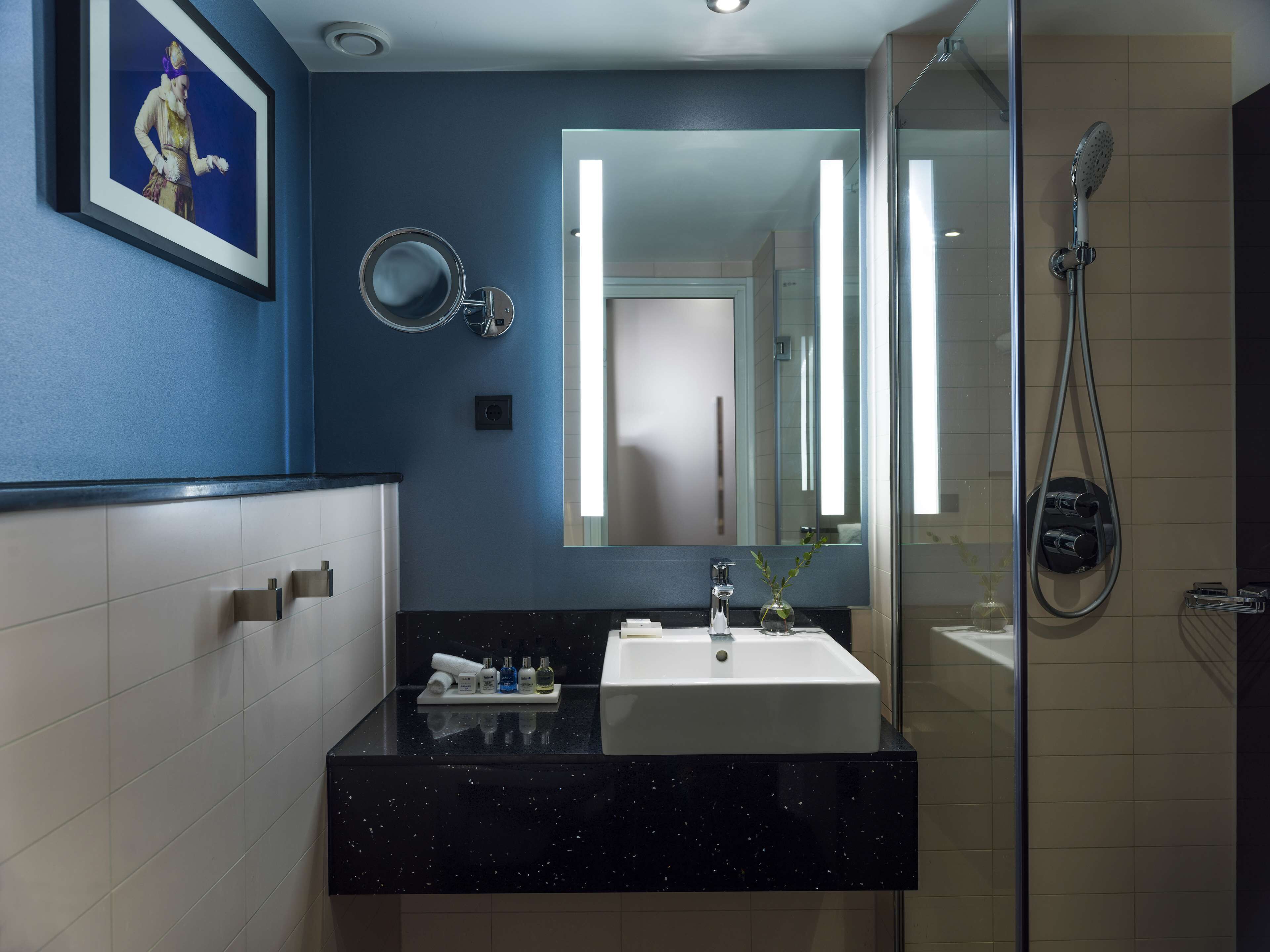Un baño moderno con encimera negra, lavamanos blanco y cabina de ducha con mampara de vidrio.