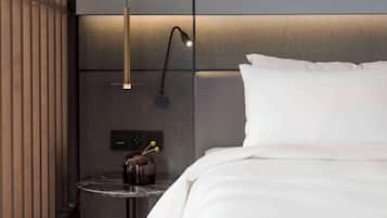 Una habitación de hotel moderna con una cama bien hecha, una pequeña mesa redonda con un florero, una lámpara de pared y un panel de pared con textura.