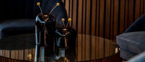 A modern interior with a round glass table, two black vases with yellow tops, and a dark blue sofa.