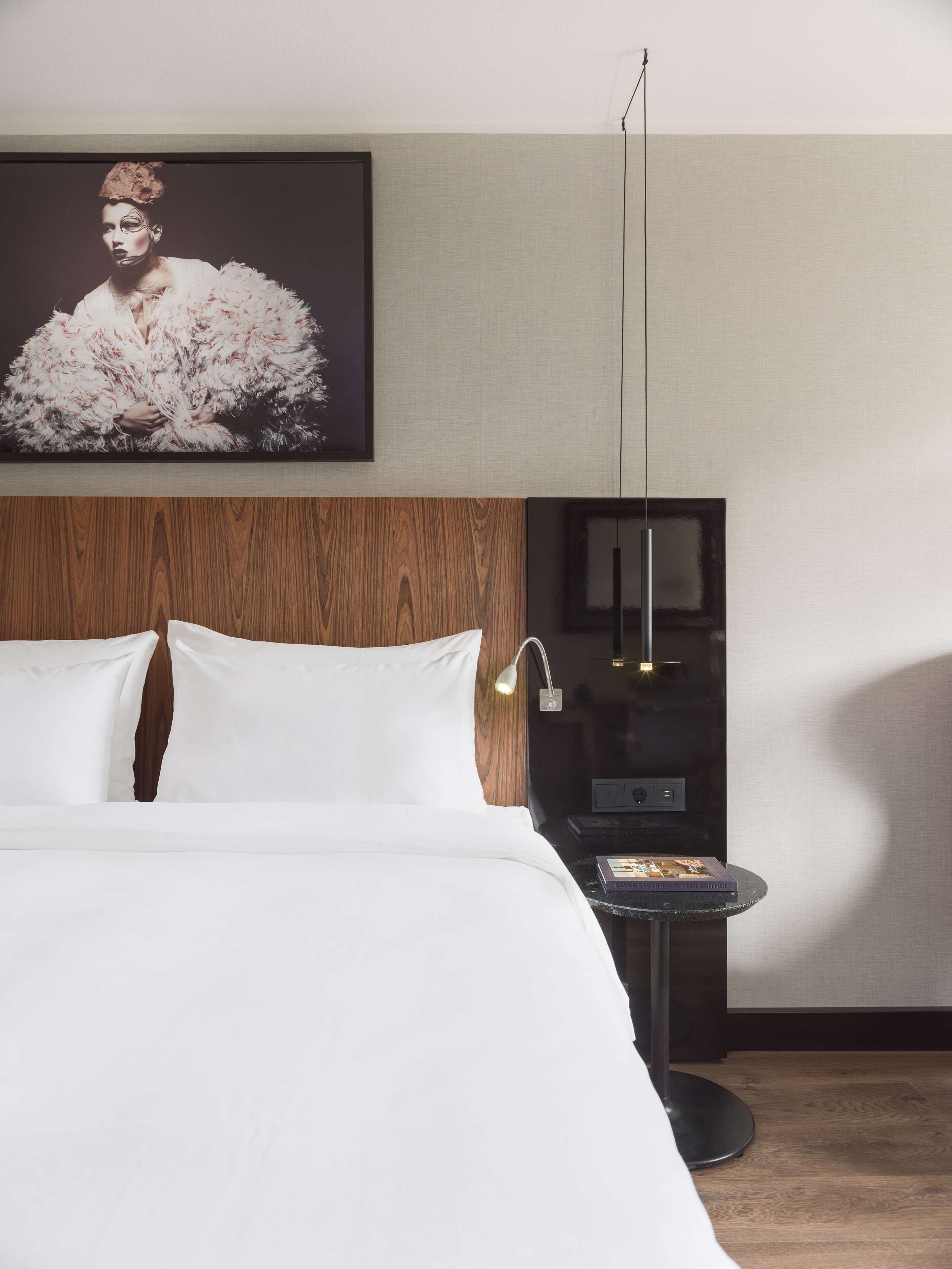 Une chambre d’hôtel avec un grand lit, une tête de lit en bois, une table de chevet avec une lampe et un tableau encadré au mur.