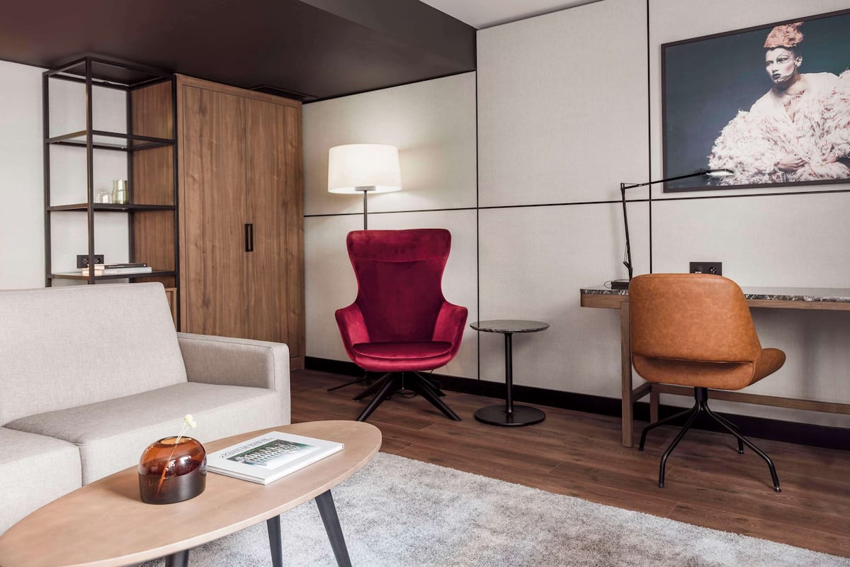 Un salon moderne comprenant un canapé, un fauteuil rouge, une table basse, un téléviseur fixé au mur et un meuble en bois.