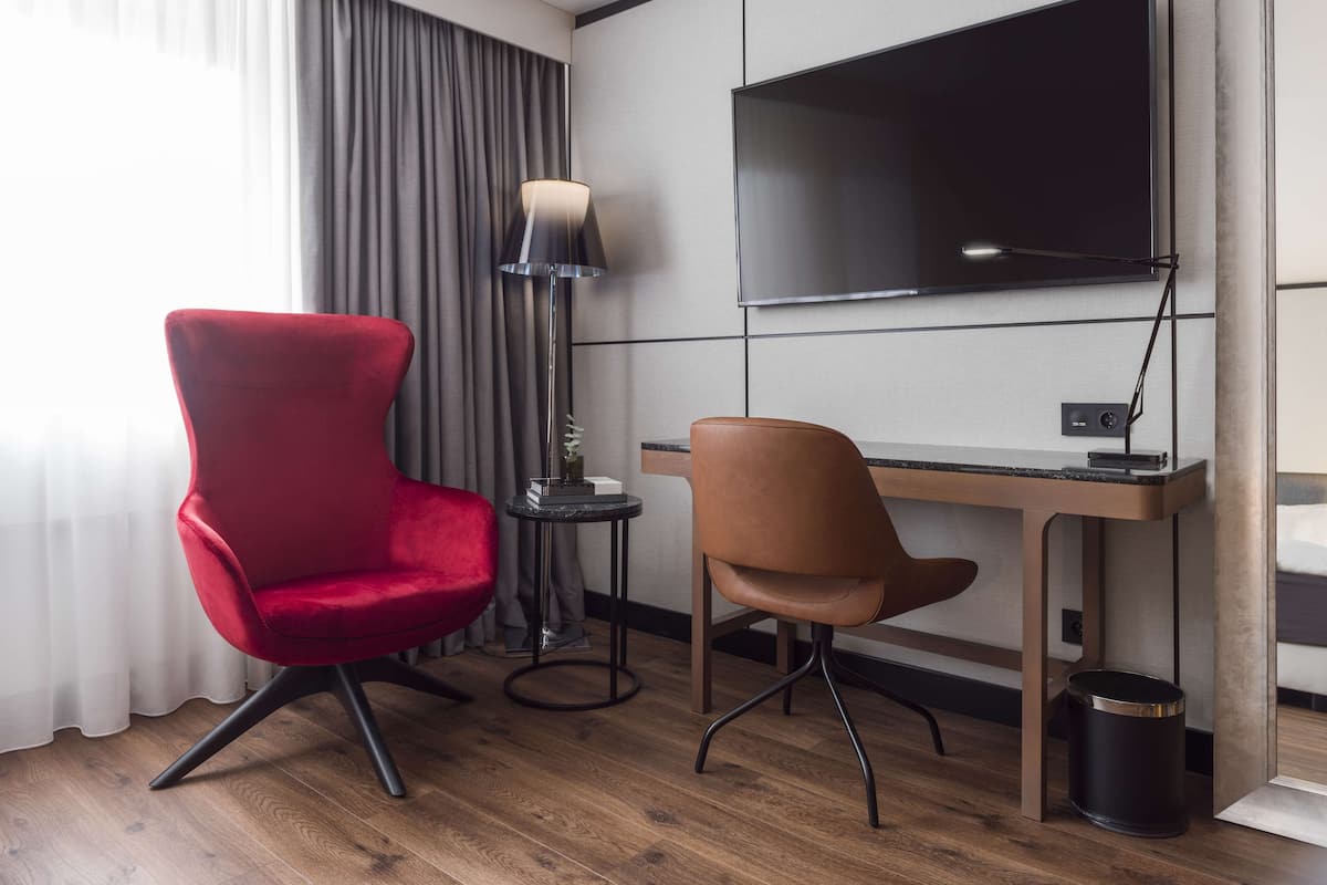Une chambre d’hôtel avec un bureau en bois, deux chaises, une télévision, une lampe et une poubelle.