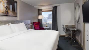 Una habitación de hotel con una cama grande, una silla roja, un escritorio con espejo y un televisor en la pared.