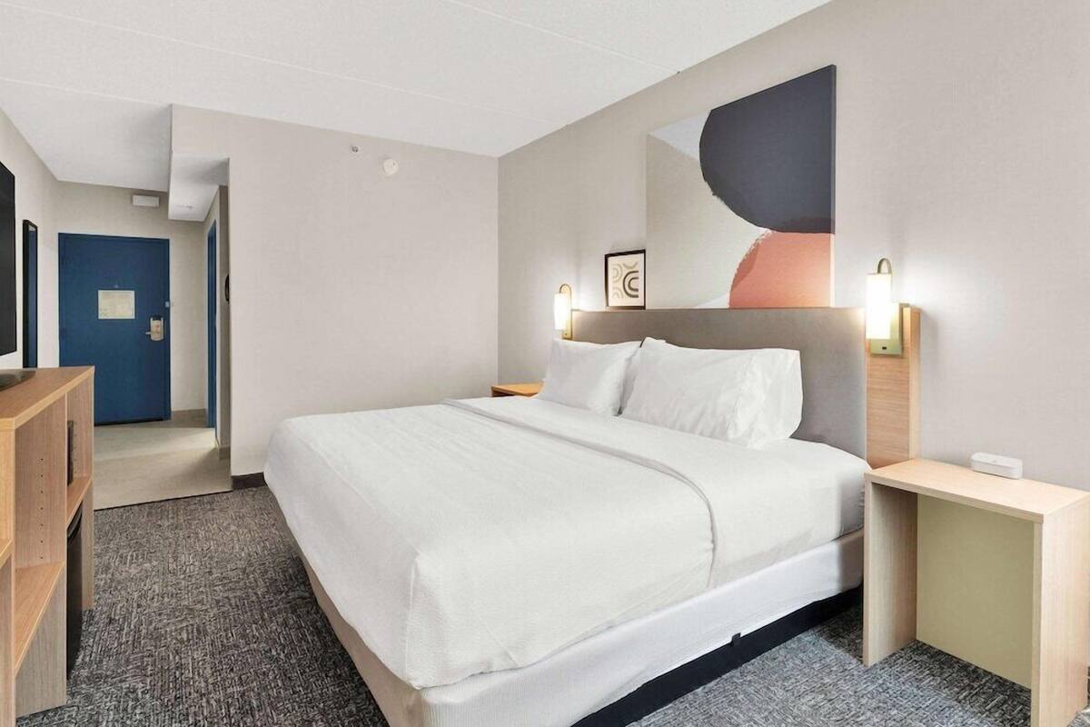 A hotel room with a bed, bedside tables, a desk, a chair, a door, and a hallway.