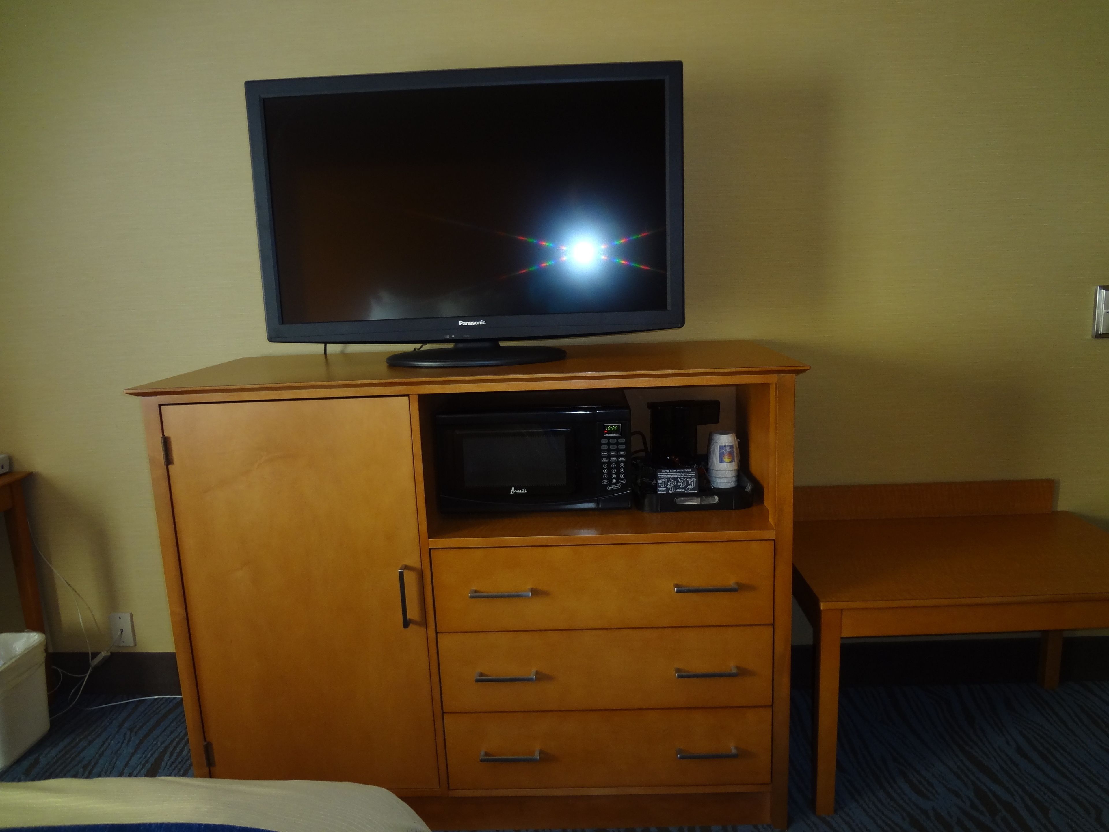 A wooden cabinet with a television on top, a microwave, and a coffee maker inside.