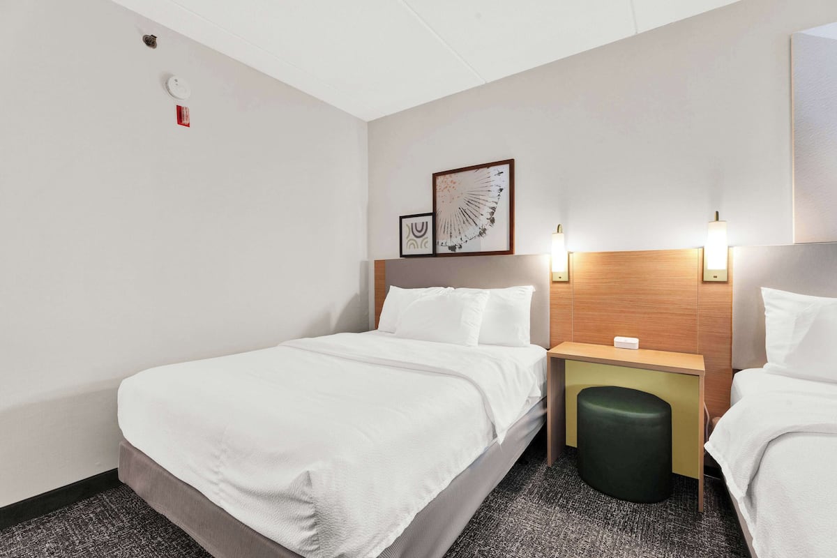 Een hotelkamer met een bed, nachtkastje, een klein tafeltje en een wandlamp.
