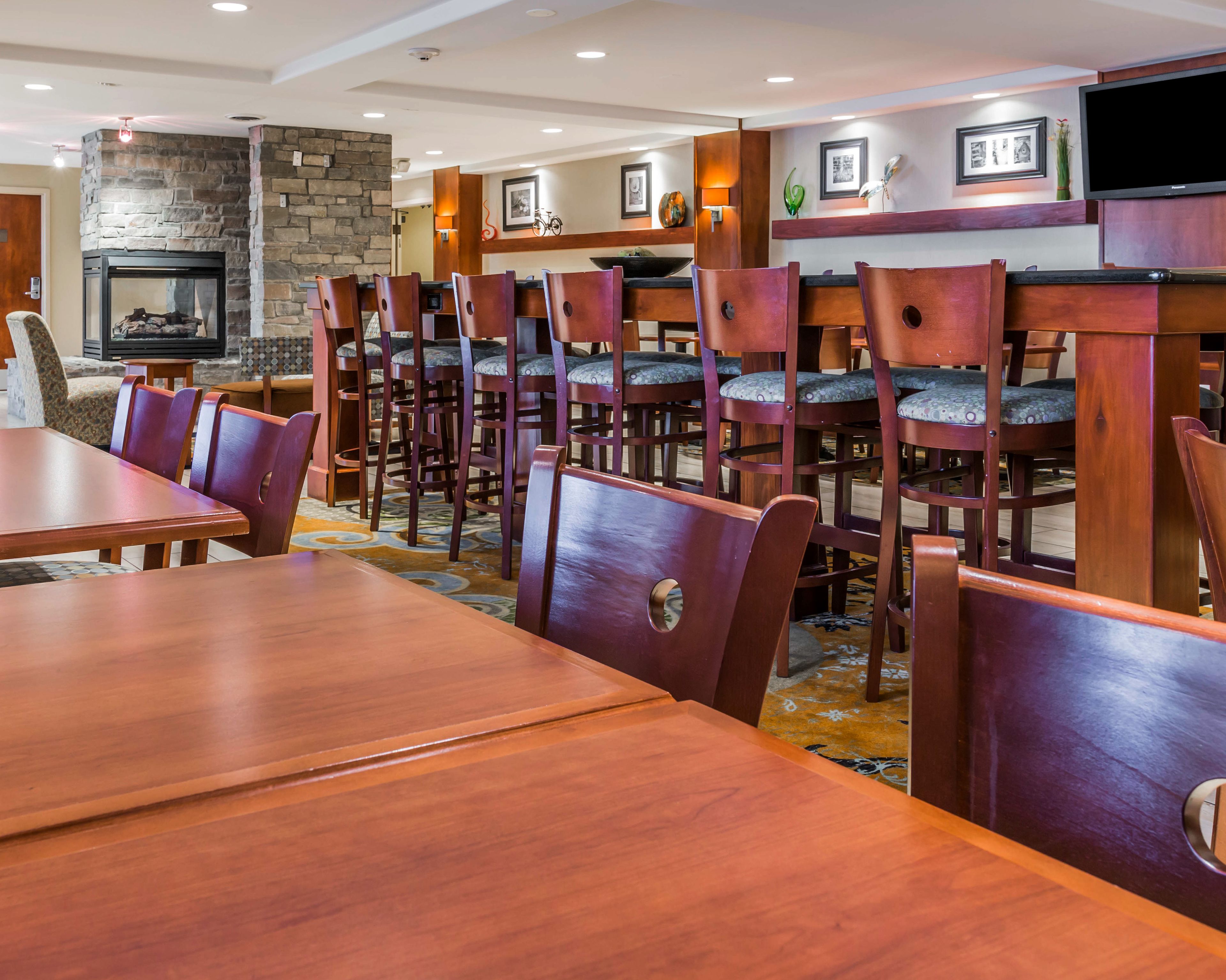 A hotel dining area with wooden tables and chairs, a stone fireplace, and a television mounted on the wall.