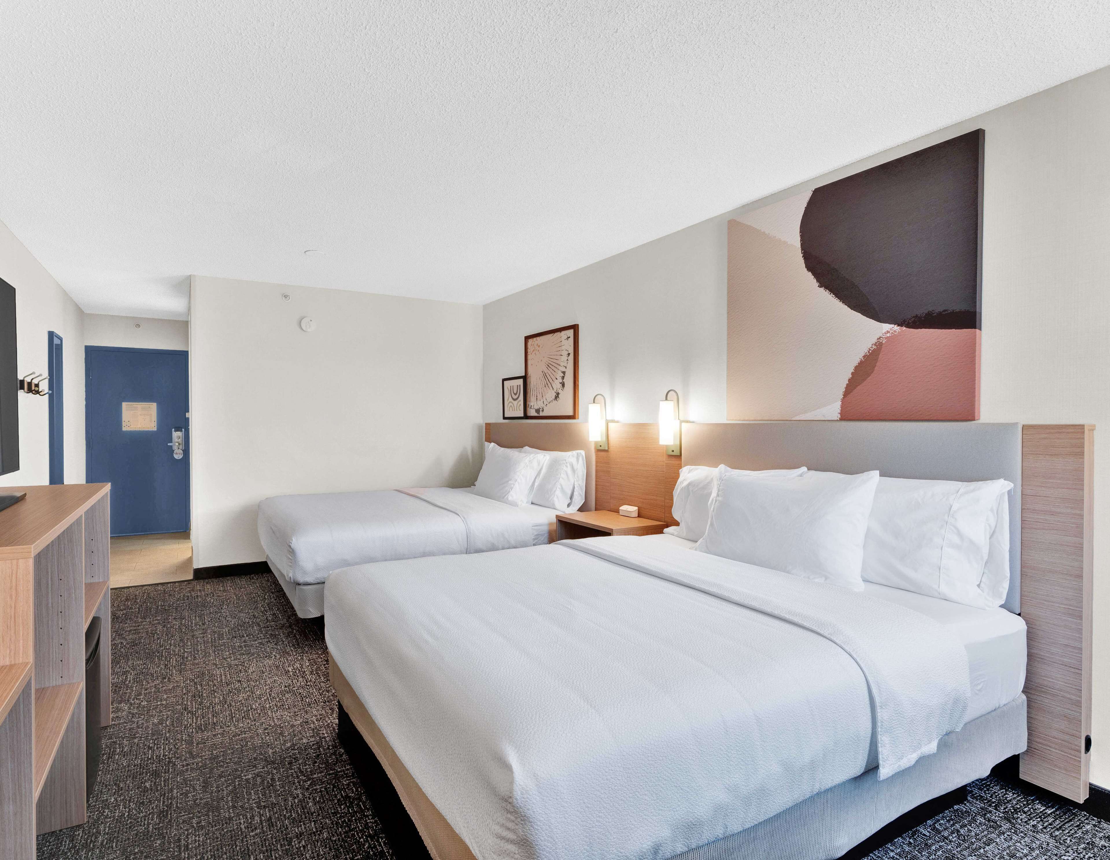 Une chambre d’hôtel avec deux lits, un bureau, une commode et un grand tableau abstrait accroché au mur.