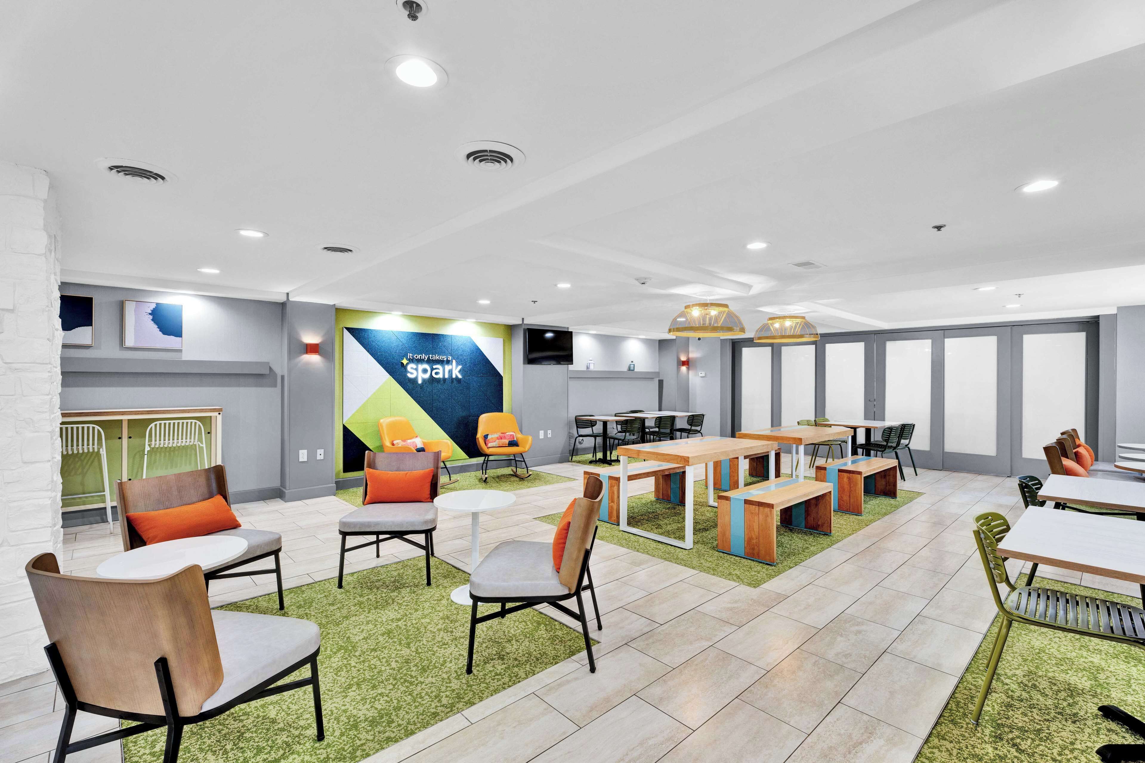 A modern indoor space with multiple seating areas, including tables and chairs, and a large wall with a 'Spark' advertisement.