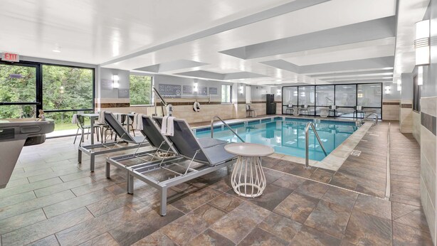 A modern indoor pool area with lounge chairs, a pool table, and a sign indicating no lifeguard on duty. - Spark by Hilton Plymouth (Plymouth)