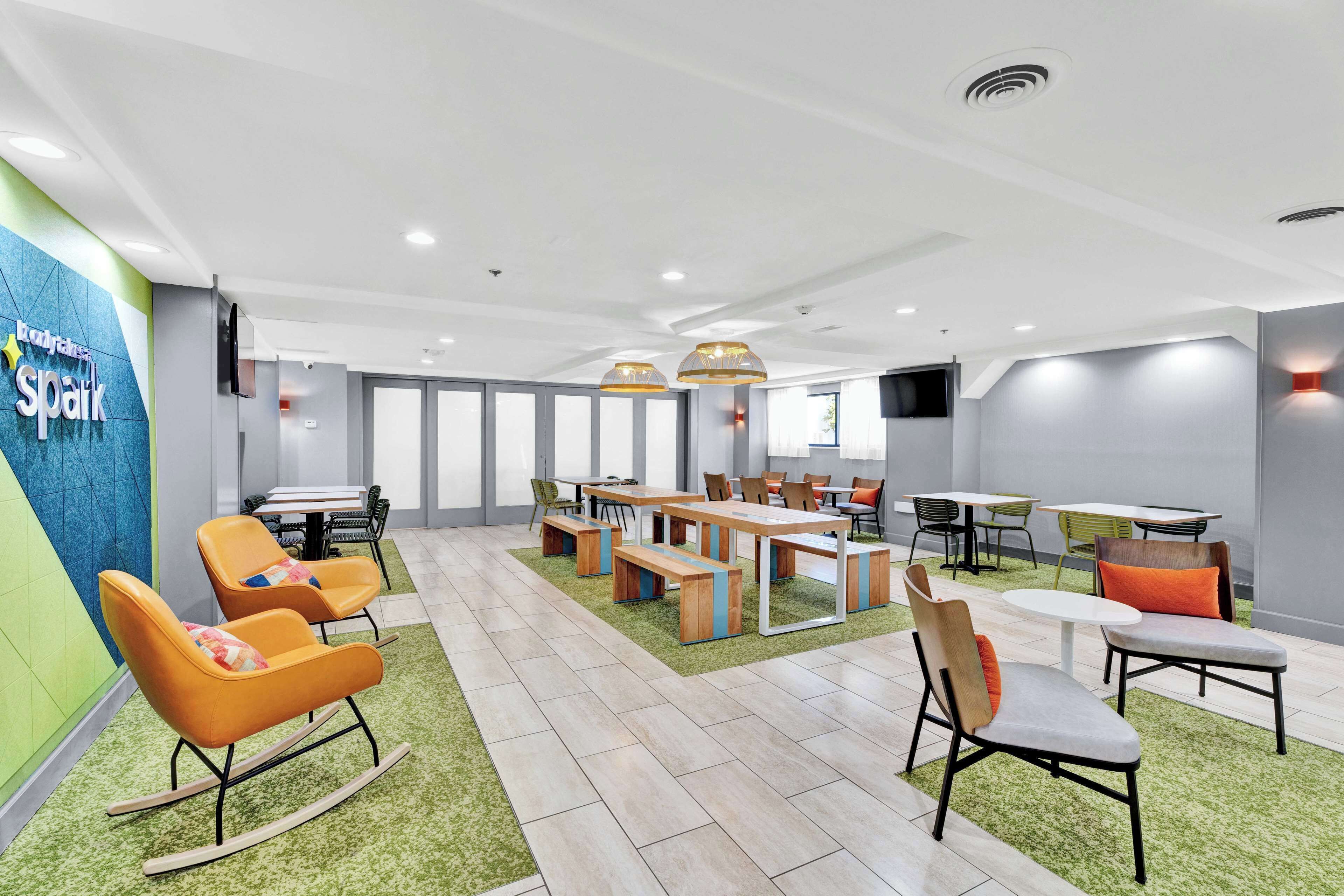 A modern conference room with a green carpet, wooden tables, and orange chairs.