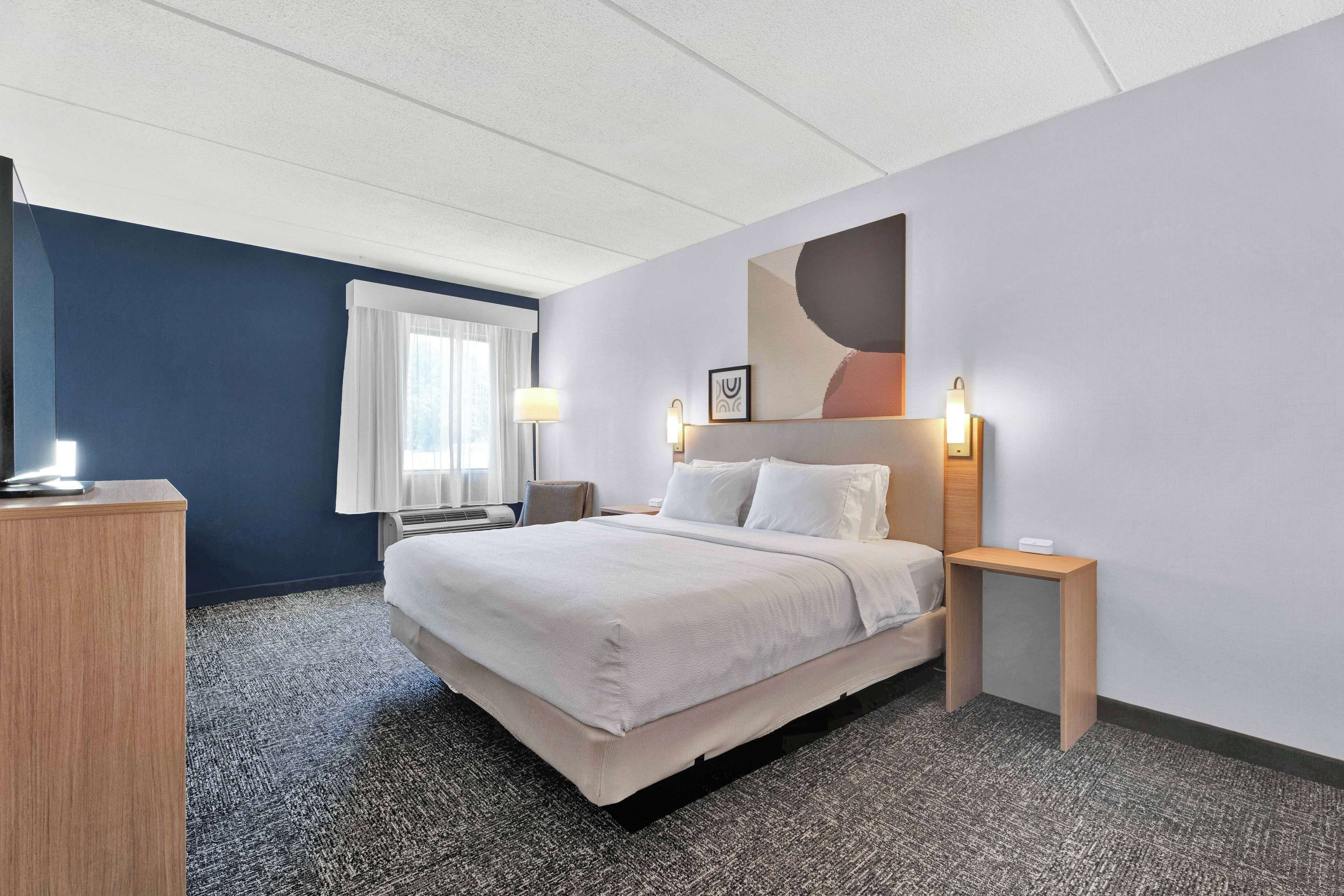 Una camera d'albergo con un letto grande, comodini, una scrivania e una finestra con tende.