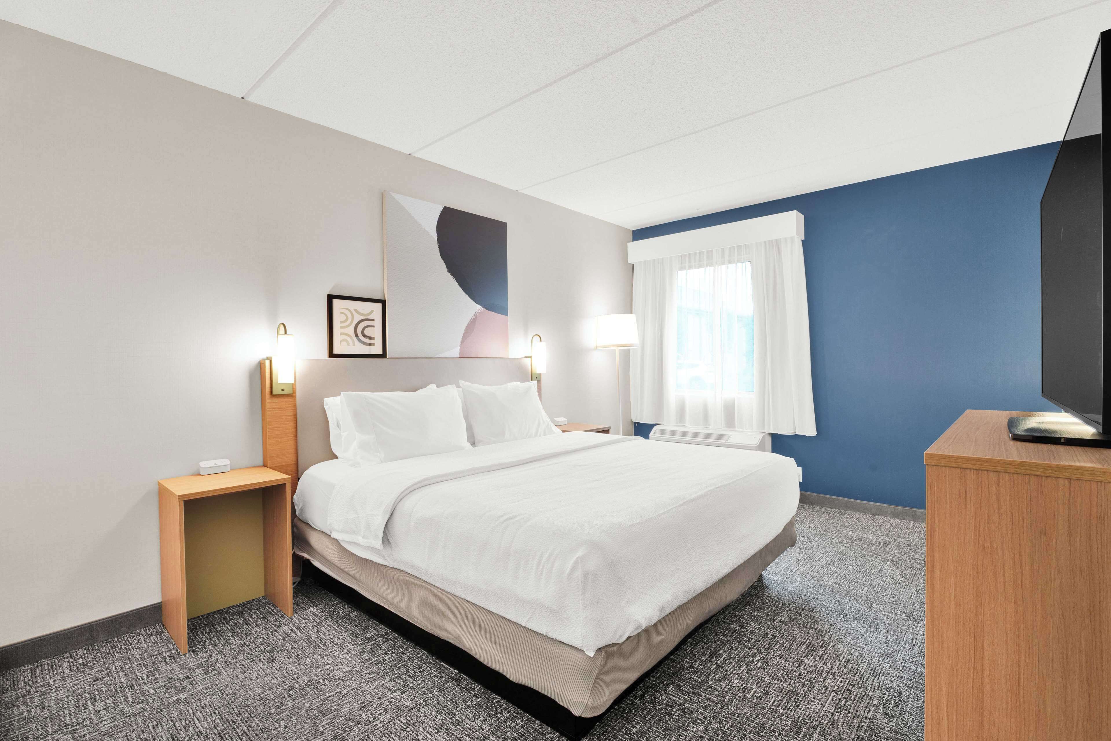 Een hotelkamer met een groot bed, een nachtkastje, een bureau, een televisie en een schilderij aan de muur.