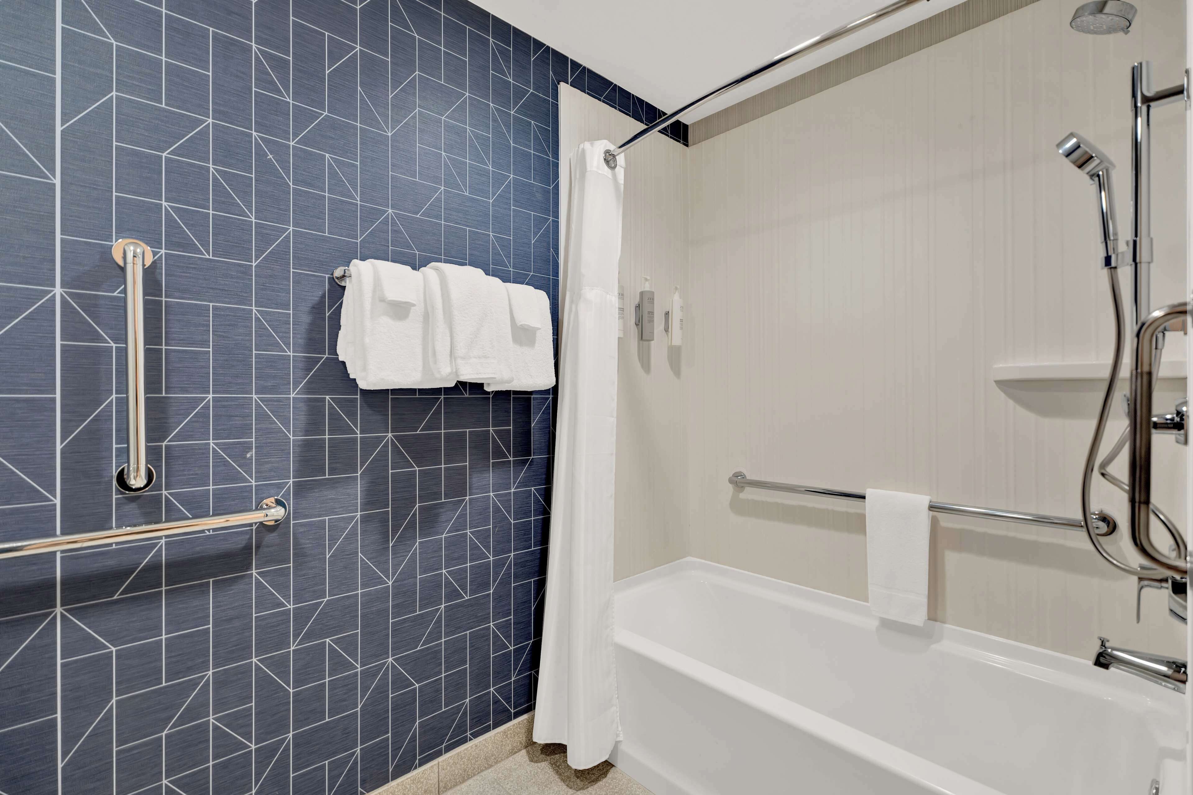A bathroom with a shower, a handrail, and a towel rack.