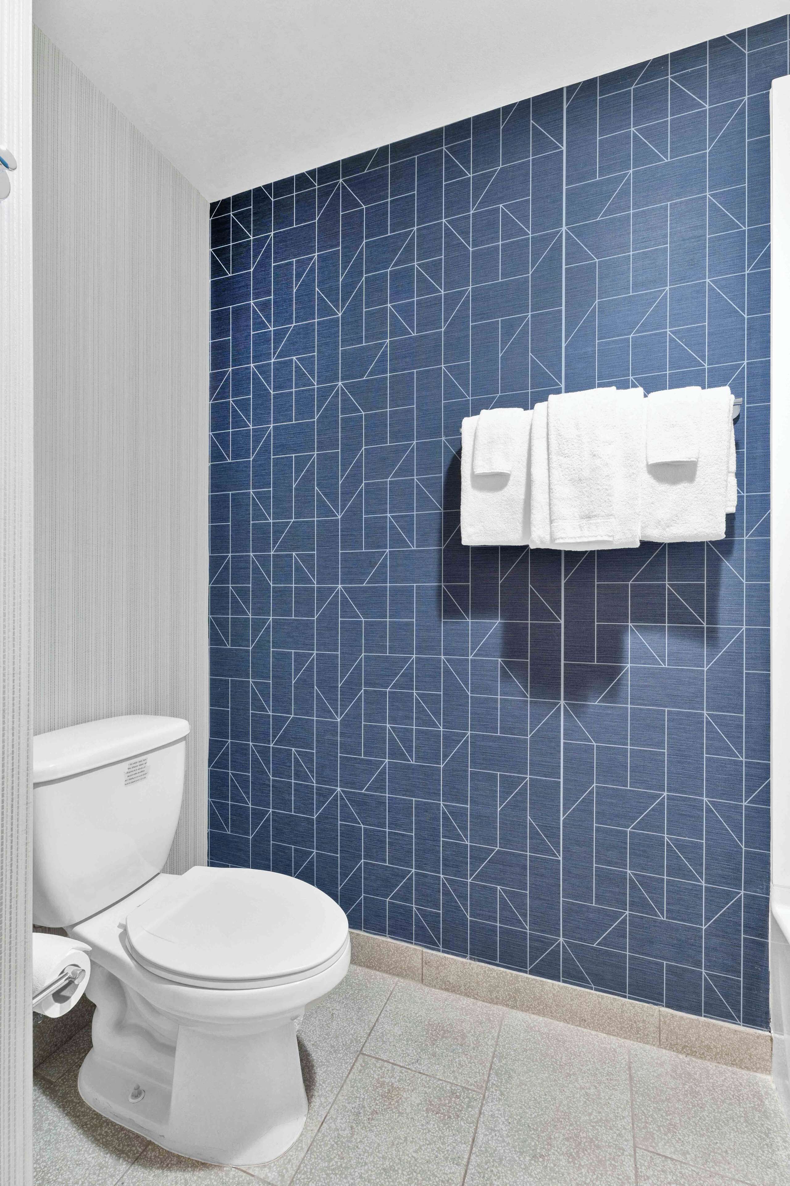 Une salle de bain avec des toilettes blanches, un mur recouvert de carreaux bleus et un porte-serviettes avec deux serviettes.