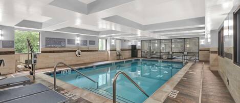 En moderne indendørs swimmingpool med tydelig skiltning, en redningsstation og et solbelyst område med siddepladser.